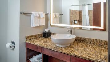 A bathroom with a granite countertop, a white vessel sink, a mirror, and a towel rack.