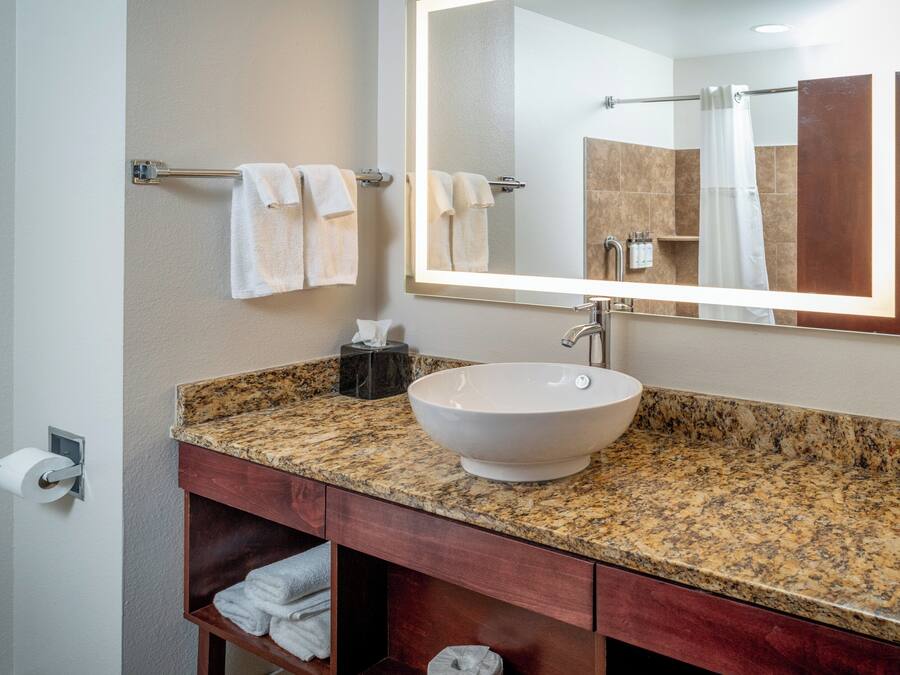 A bathroom with a granite countertop, a white vessel sink, a mirror, and a towel rack.