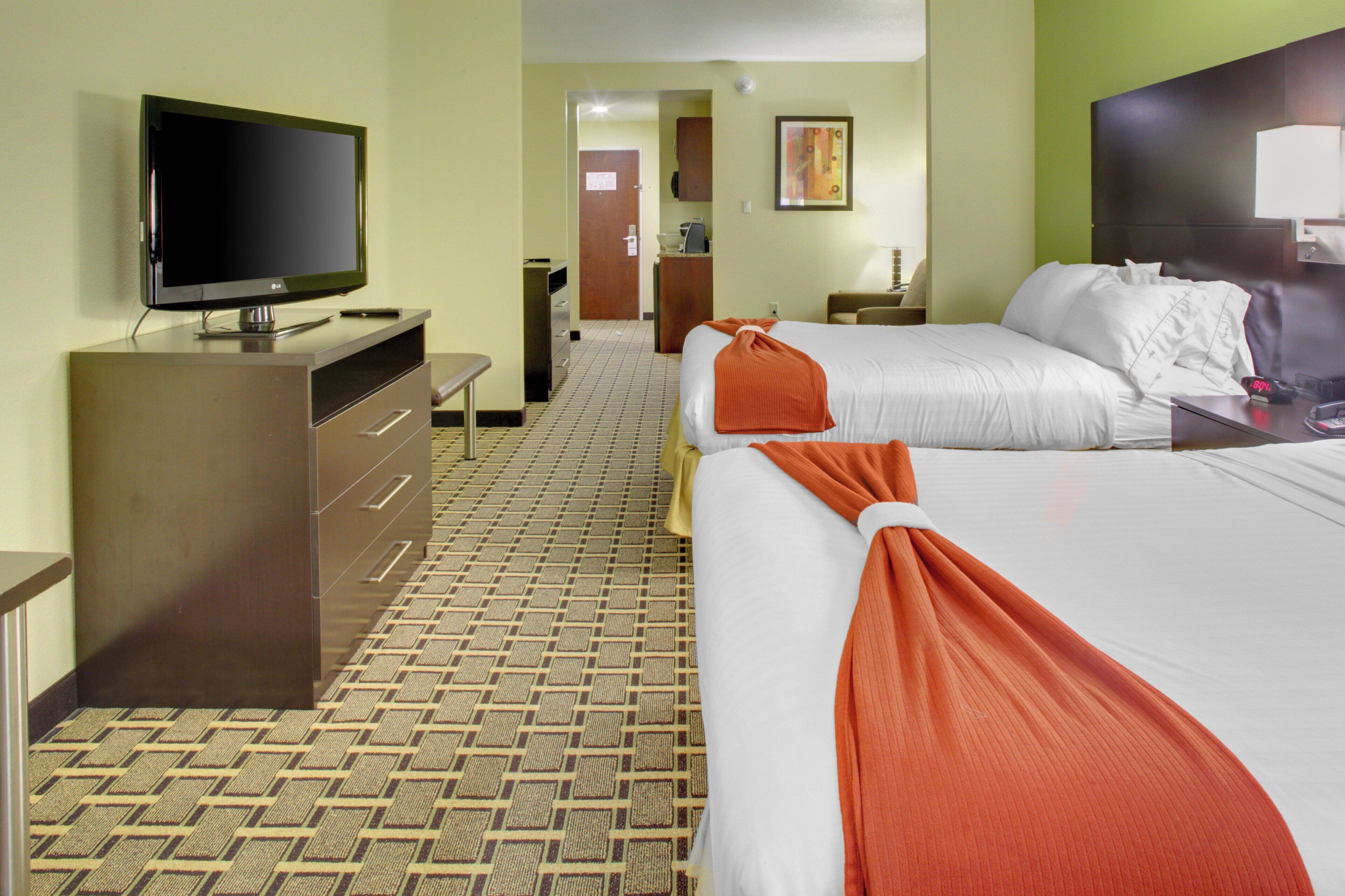 Habitación de hotel con dos camas, televisión, escritorio y baño visible a través de una puerta abierta.