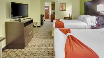 Habitación de hotel con dos camas, televisión, escritorio y baño visible a través de una puerta abierta.