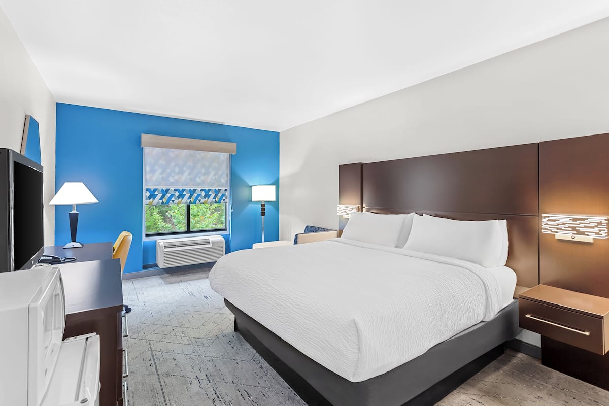 A modern hotel room with a large bed, bedside tables, a desk, and a window with a view of greenery.