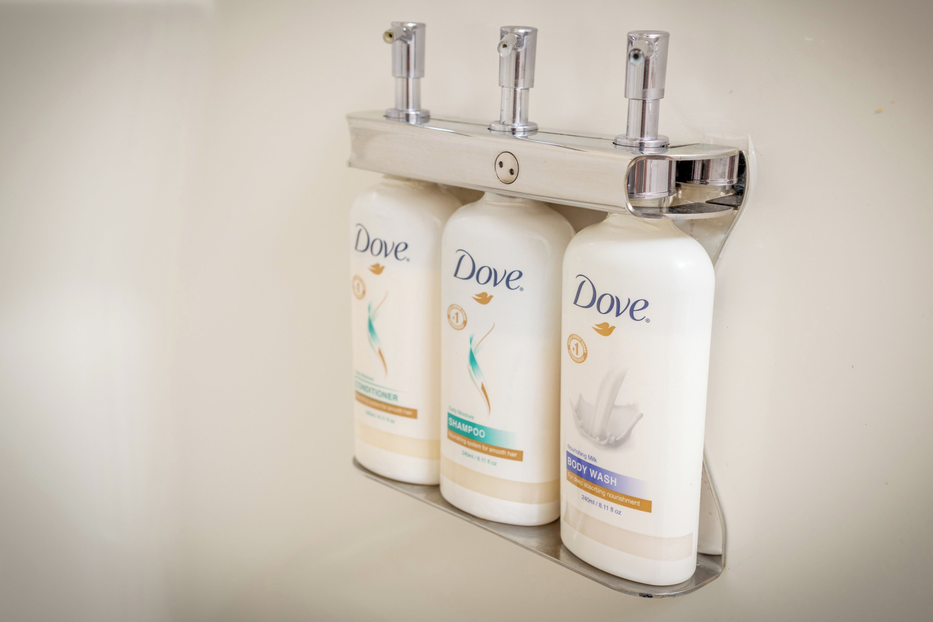 Three Dove body wash bottles on a metal shelf.