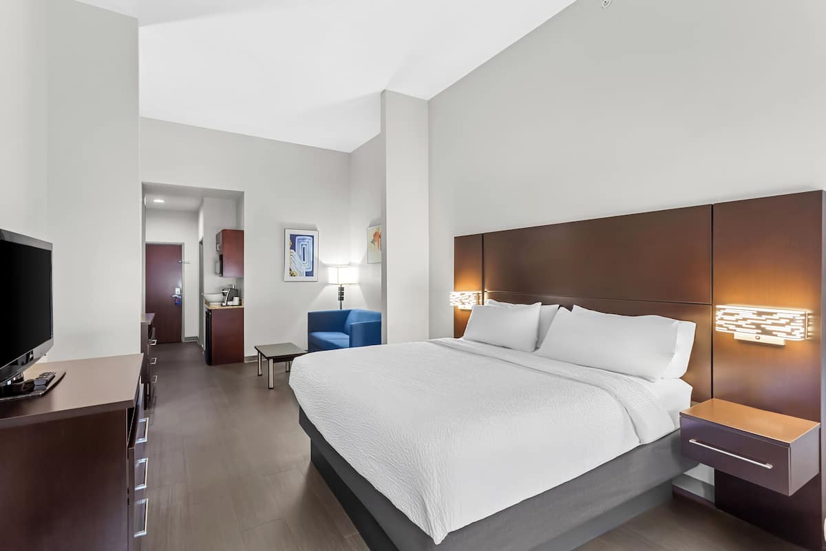 A modern hotel room with a large bed, a desk, a TV, and a bathroom visible through an open door.