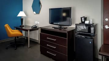 A hotel room with a desk, a television, a microwave, a coffee maker, and a chair.