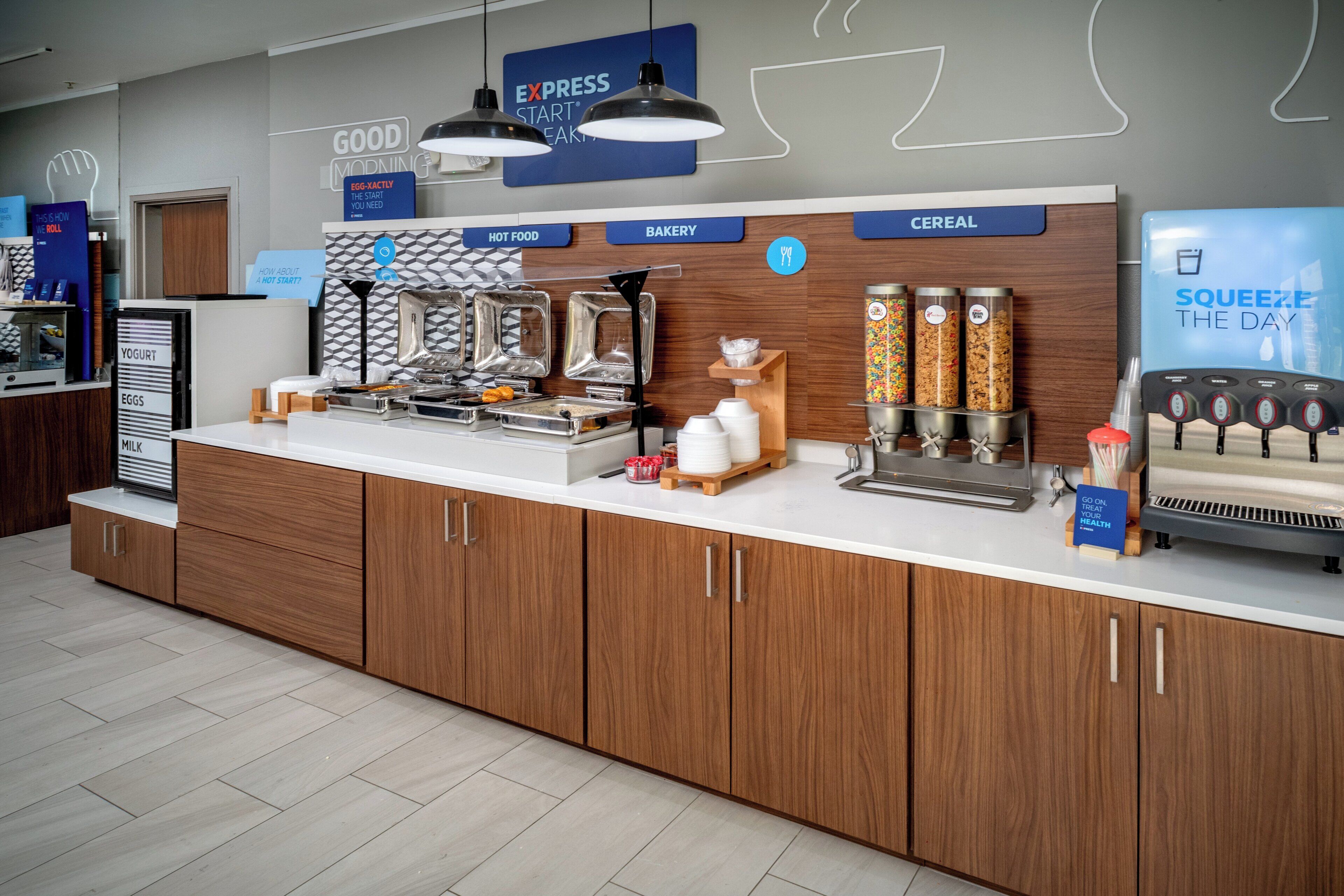 A breakfast bar with labeled dispensers for yogurt, eggs, milk, hot food, bakery, and cereal.