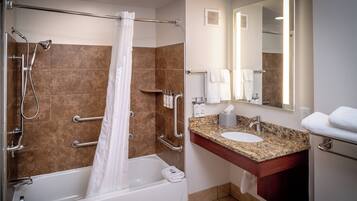 A modern bathroom with a walk-in shower, grab bars, a vanity with a sink, and a large mirror.