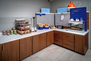 Estación de desayuno con diversas opciones de comida, incluyendo frutas, pasteles y una máquina de café.
