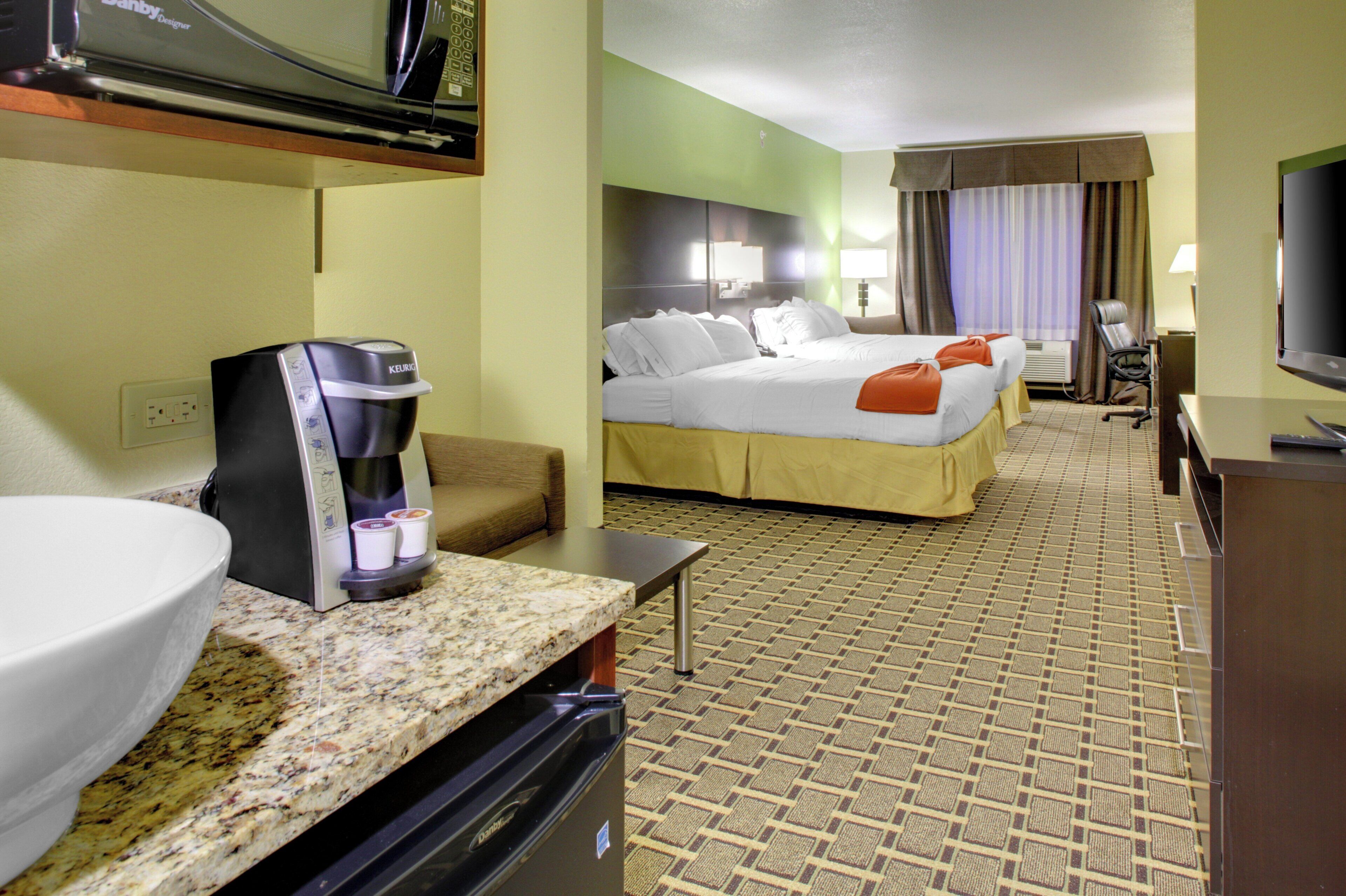 A hotel room with a bed, a coffee maker, a TV, and a desk with a computer.