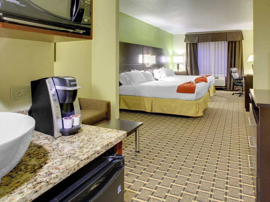 A hotel room with a bed, a coffee maker, a TV, and a desk with a computer.