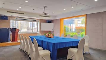 Un salón de conferencias con una larga mesa, sillas blancas, un atril y un amplio ventanal.