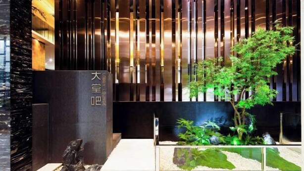 Un interior moderno con un diseño de paneles de madera verticales, una gran estructura de piedra negra con caracteres chinos y un pequeño jardín interior con un bonsái.