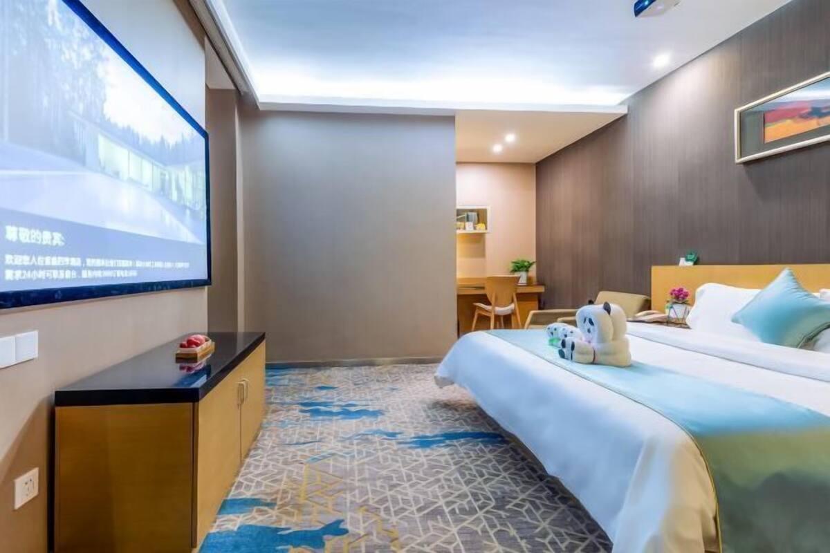 A hotel room with a bed, a desk, and a TV screen displaying a scenic image.