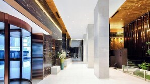 Un lobby moderno con un muro de vidrio curvo, techo de madera y una columna central.
