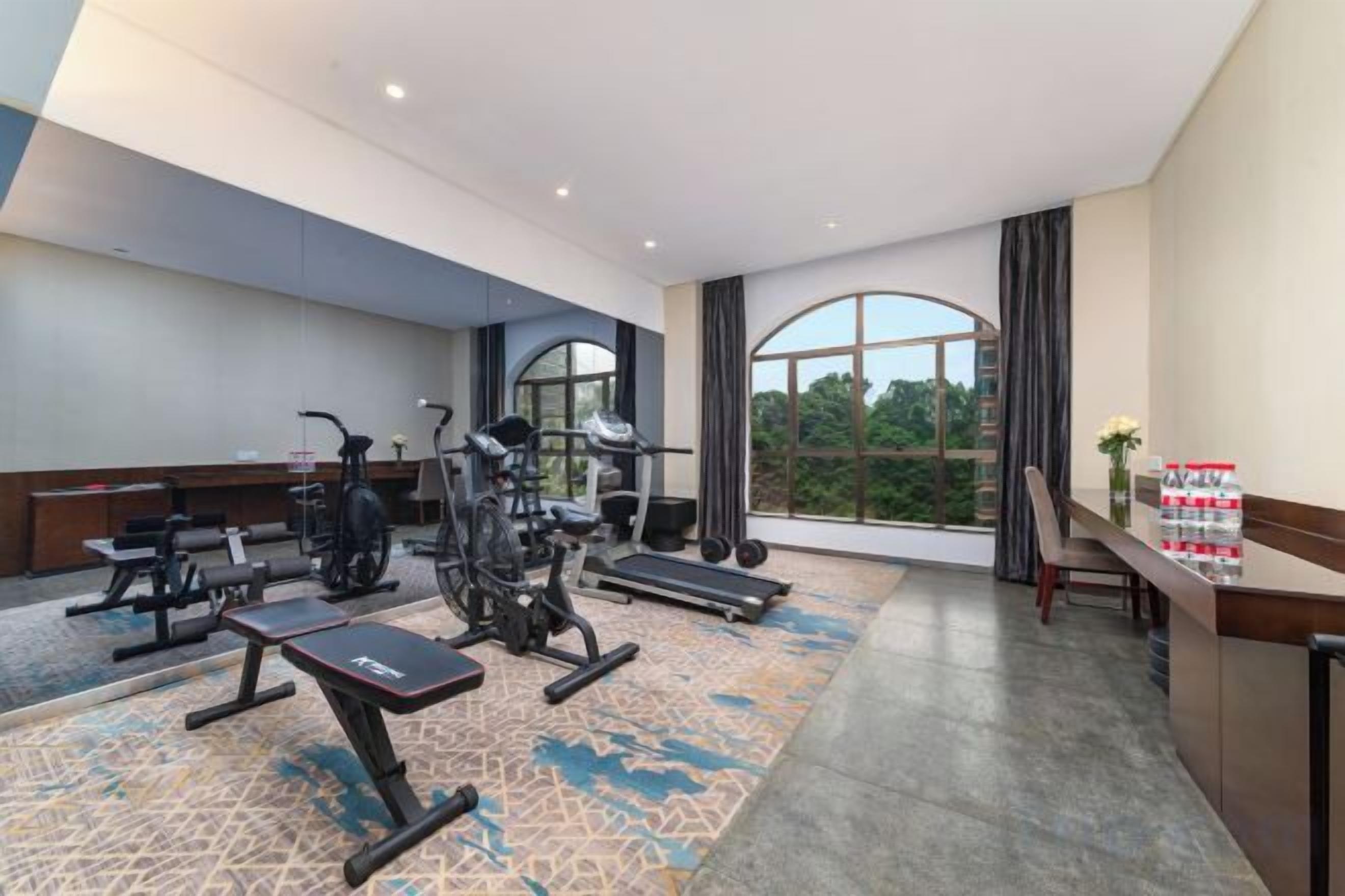 Een hotelgymzaal met trainingsapparatuur, een groot raam en uitzicht op bomen.