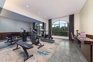 Gimnasio de hotel con equipo de ejercicio, un ventanal y vista a árboles.