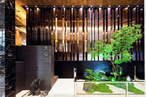 A reception area with a modern design, featuring a vertical wooden panel, a reception desk, and a small indoor garden. - Elong ME Hotel (Changsha Zhongmao City) (Changsha)