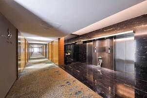 A hotel corridor with a patterned carpet, a wall-mounted plant, and a modern elevator.