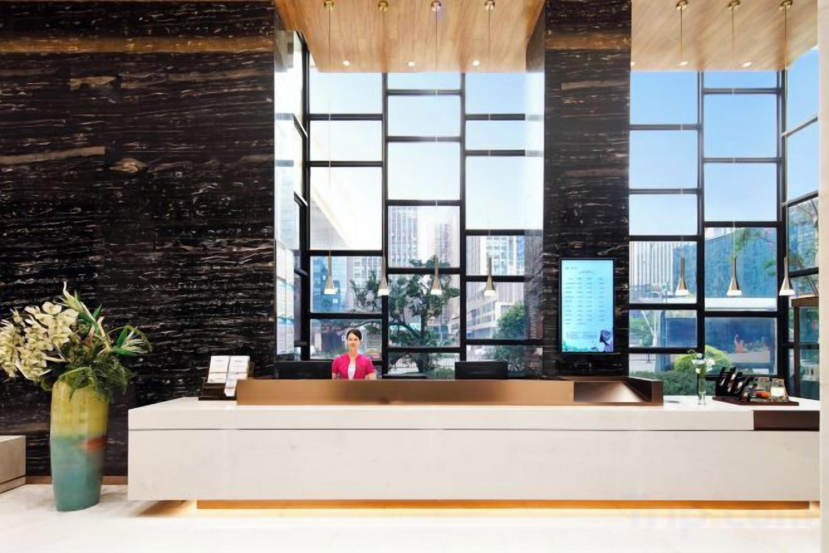 Un mostrador de recepción con un amplio ventanal, una recepcionista y una pantalla digital.