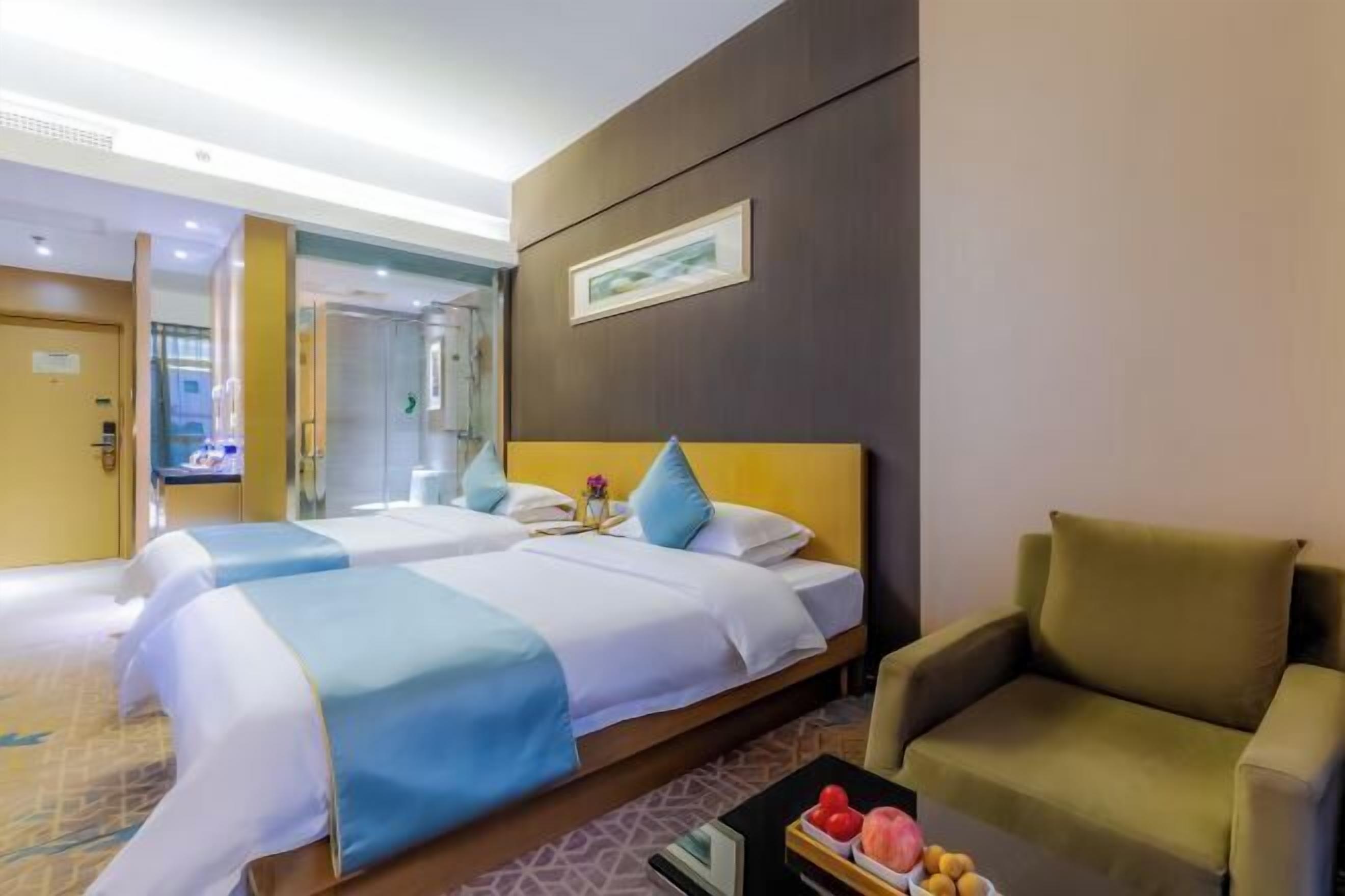A hotel room with two beds, a sofa, a coffee table with fruits, and a framed picture on the wall.