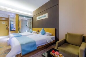 Ein Hotelzimmer mit zwei Betten, einem Sofa, einem Couchtisch mit Früchten und einem gerahmten Bild an der Wand.