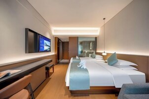 Habitación de hotel con cama, escritorio, silla, televisión y baño visible a través de una puerta de vidrio.
