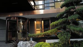 A modern building entrance with a glass door, a well-maintained garden with various shrubs, and a large rock feature.