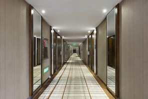 Ein langer, schmaler Hotelkorridor mit Spiegelwänden und Fliesenboden.