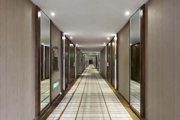 Een lange, smalle hotelgang met spiegelwanden en een betegelde vloer.