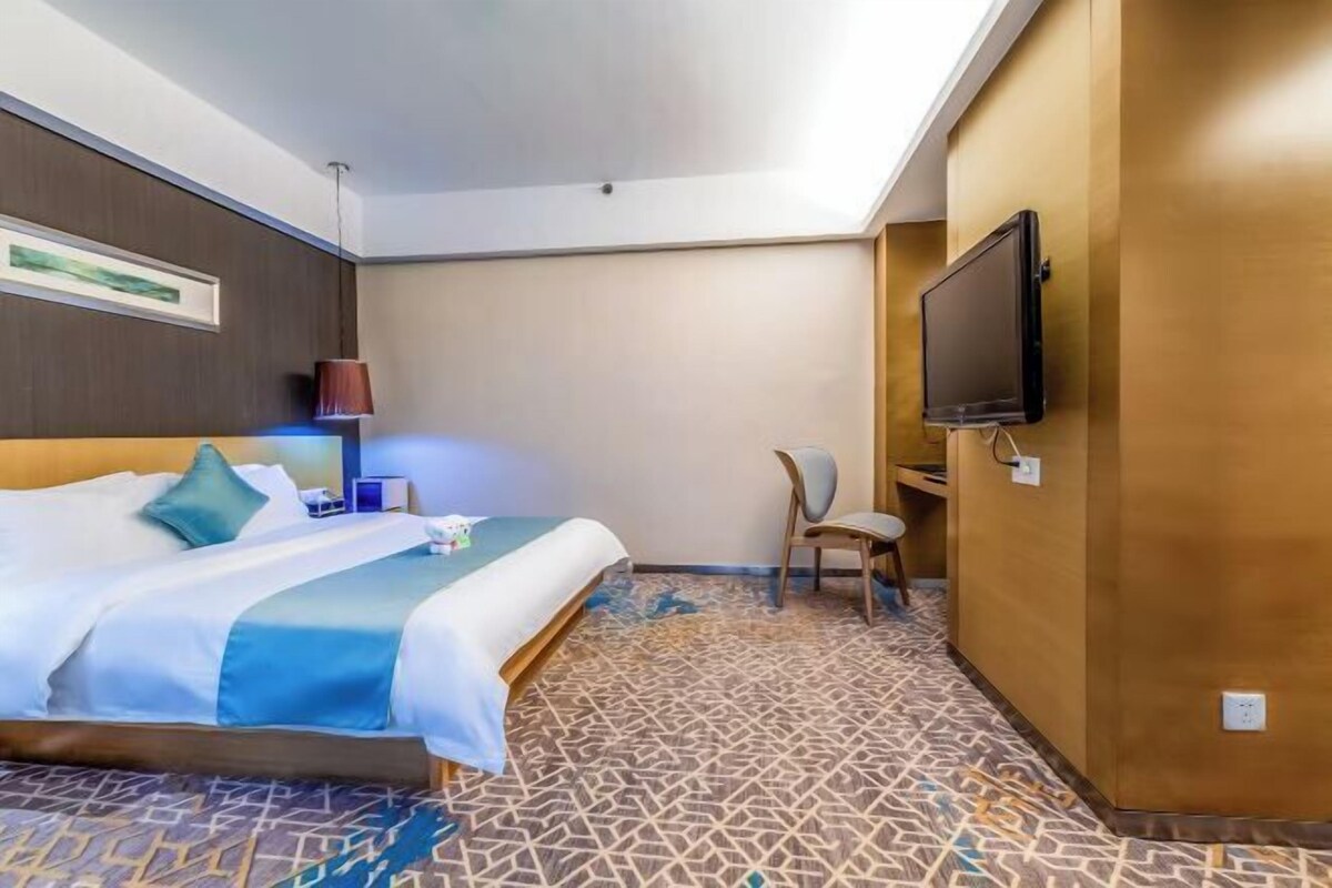 Ein Hotelzimmer mit einem Bett, einem Schreibtisch, einem Stuhl, einem Fernseher und einem gemusterten Teppich.