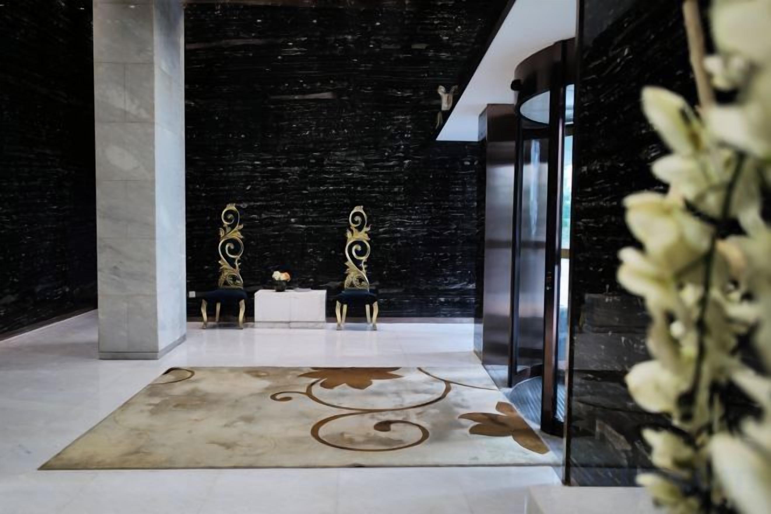 A lobby with a marble floor, two ornate chairs, a reception desk, and a glass partition.