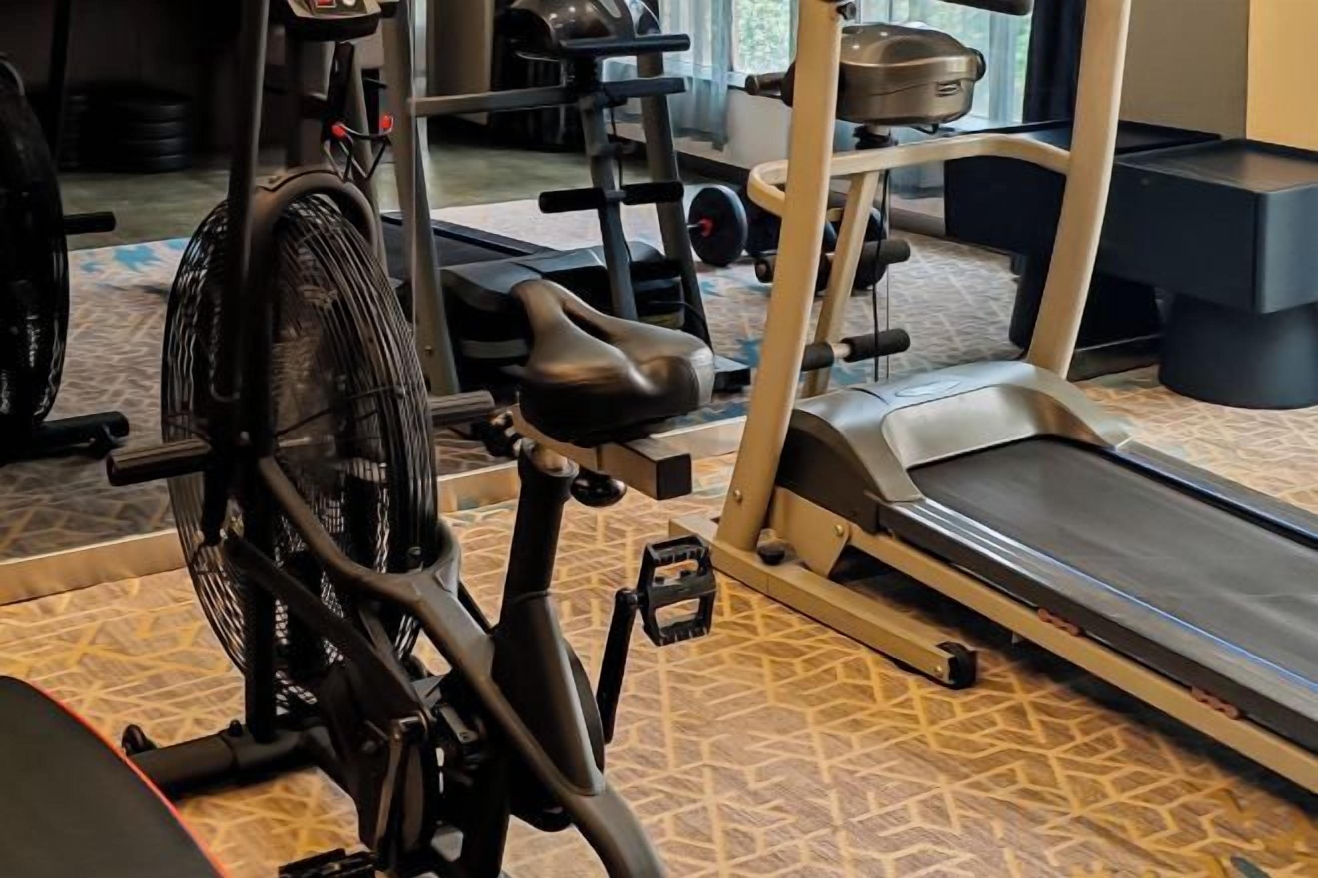 Ein stationäres Fahrrad, Laufband und Hanteln in einem Fitnessstudio.