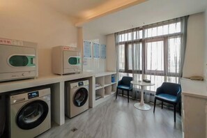 A laundry area with washing machines and dryers, a small seating area with chairs, and a window with curtains. - Elong ME Hotel (Changsha Zhongmao City) (Changsha)