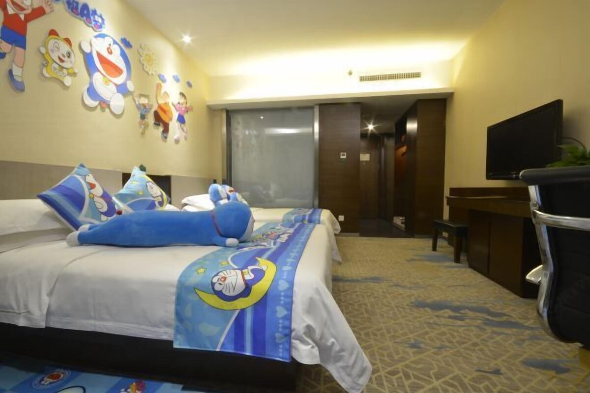 Ein Hotelzimmer mit einem Bett, das mit Cartoon-Figuren verziert ist, einem Schreibtisch mit Fernseher und einem gemusterten Teppich.