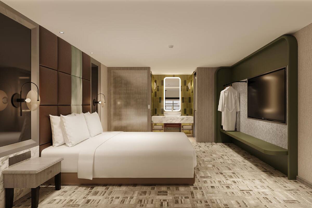 A modern hotel room with a large bed, a TV, a mirror, and a bathroom visible through an open door.