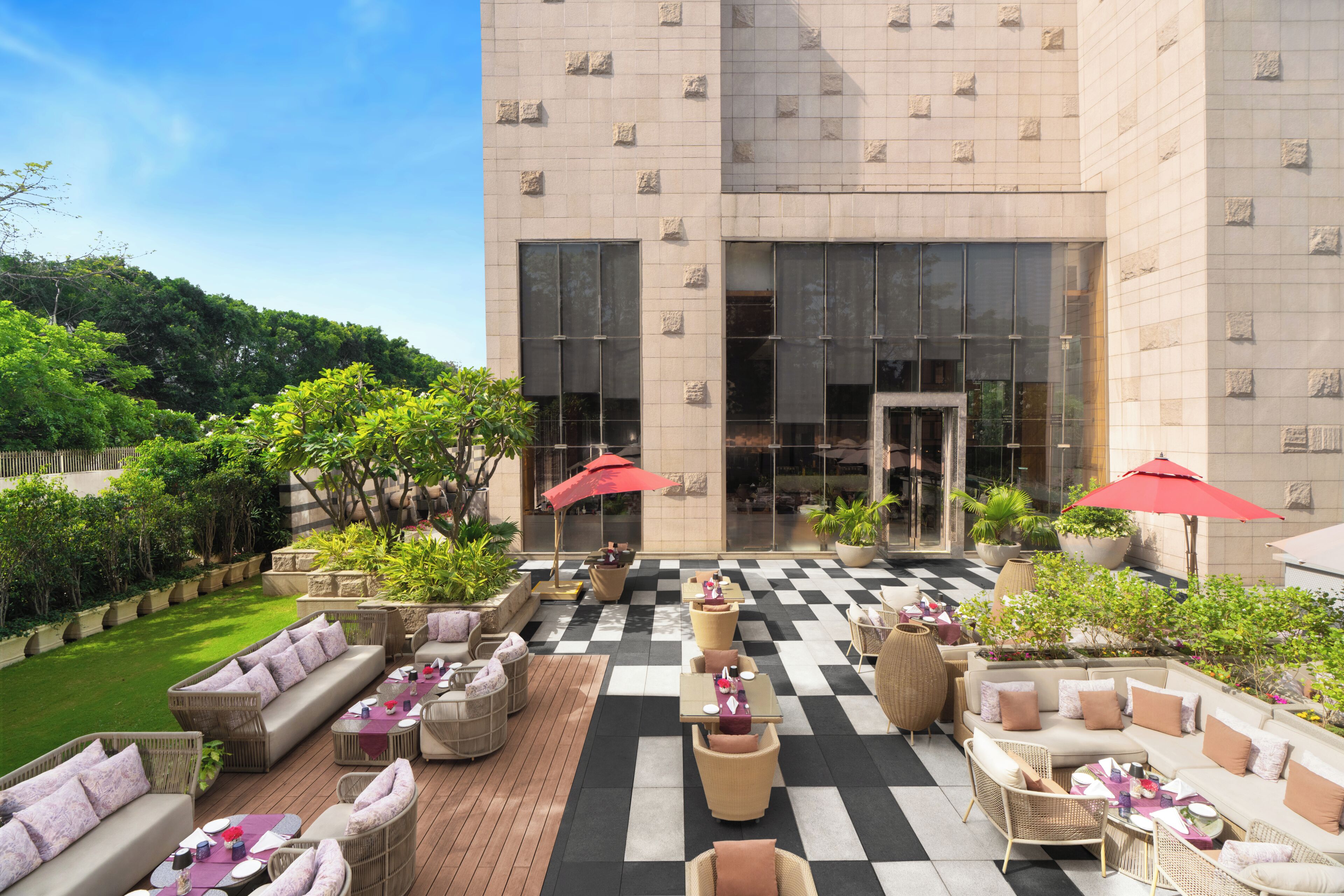 An outdoor seating area with checkered flooring, wicker furniture, and red umbrellas.