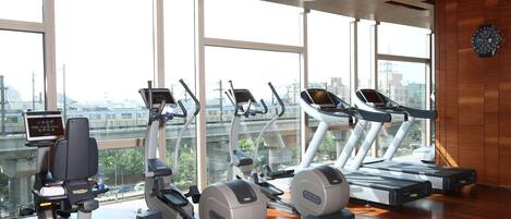 A gym with treadmills, elliptical machines, and a digital screen.