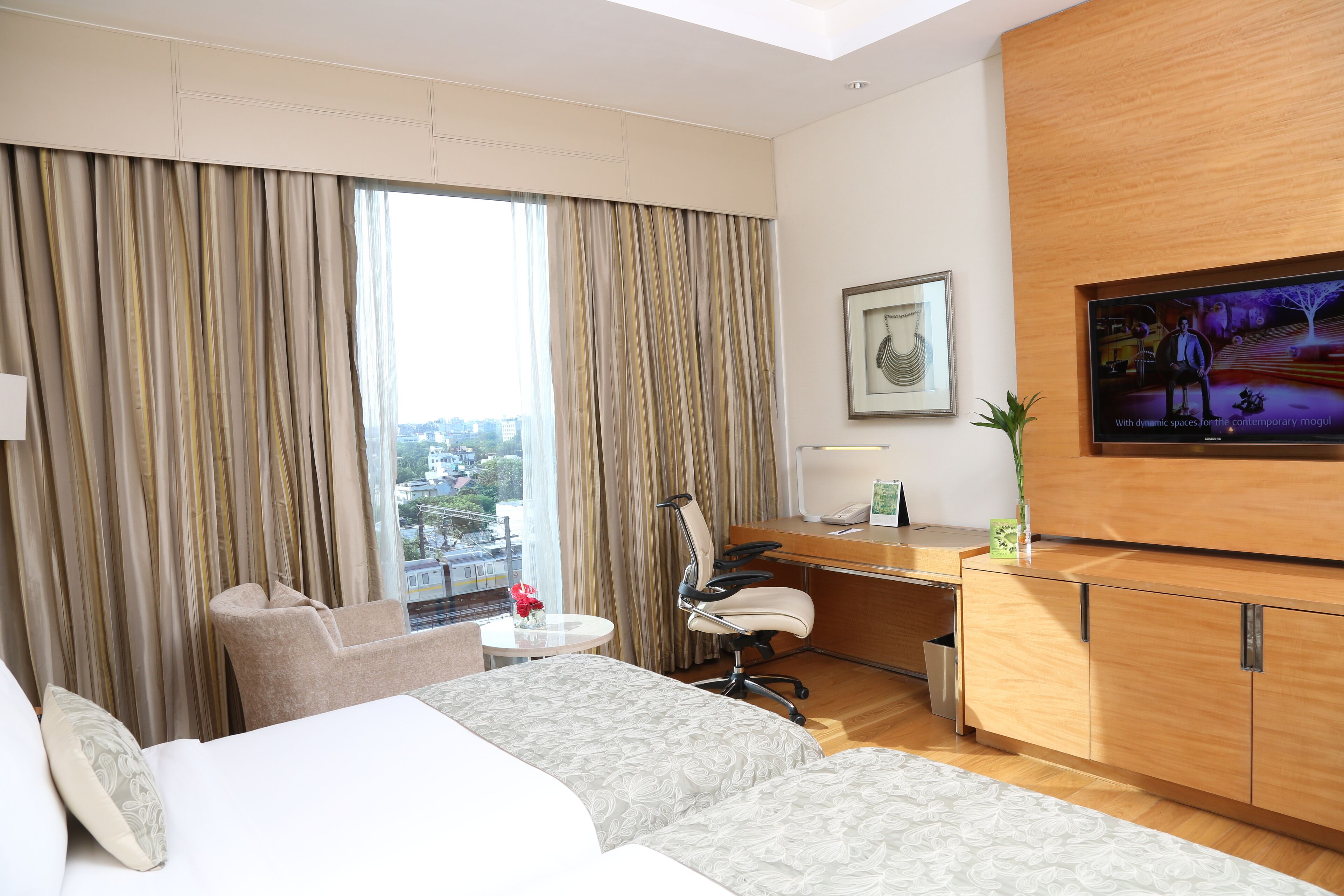 A hotel room with a bed, a desk, a chair, a TV, and a window with curtains.