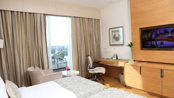 A hotel room with a bed, a desk, a chair, a TV, and a window with curtains.