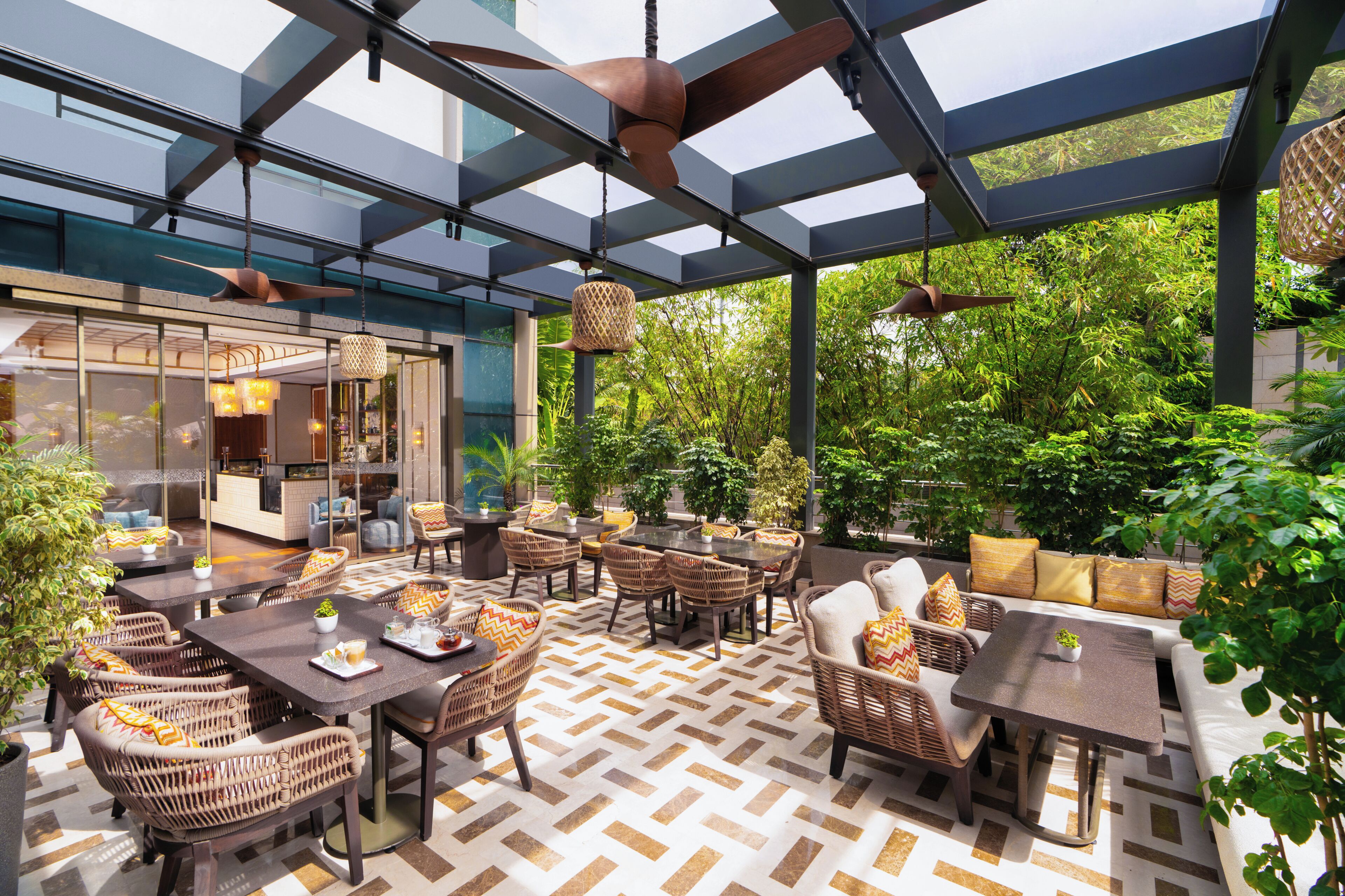 An outdoor dining area with wicker furniture, a patterned floor, and a glass ceiling.