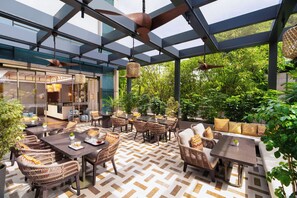 An outdoor dining area with wicker furniture, a patterned floor, and a glass ceiling. - Taj City Centre Gurugram (Gurugram)