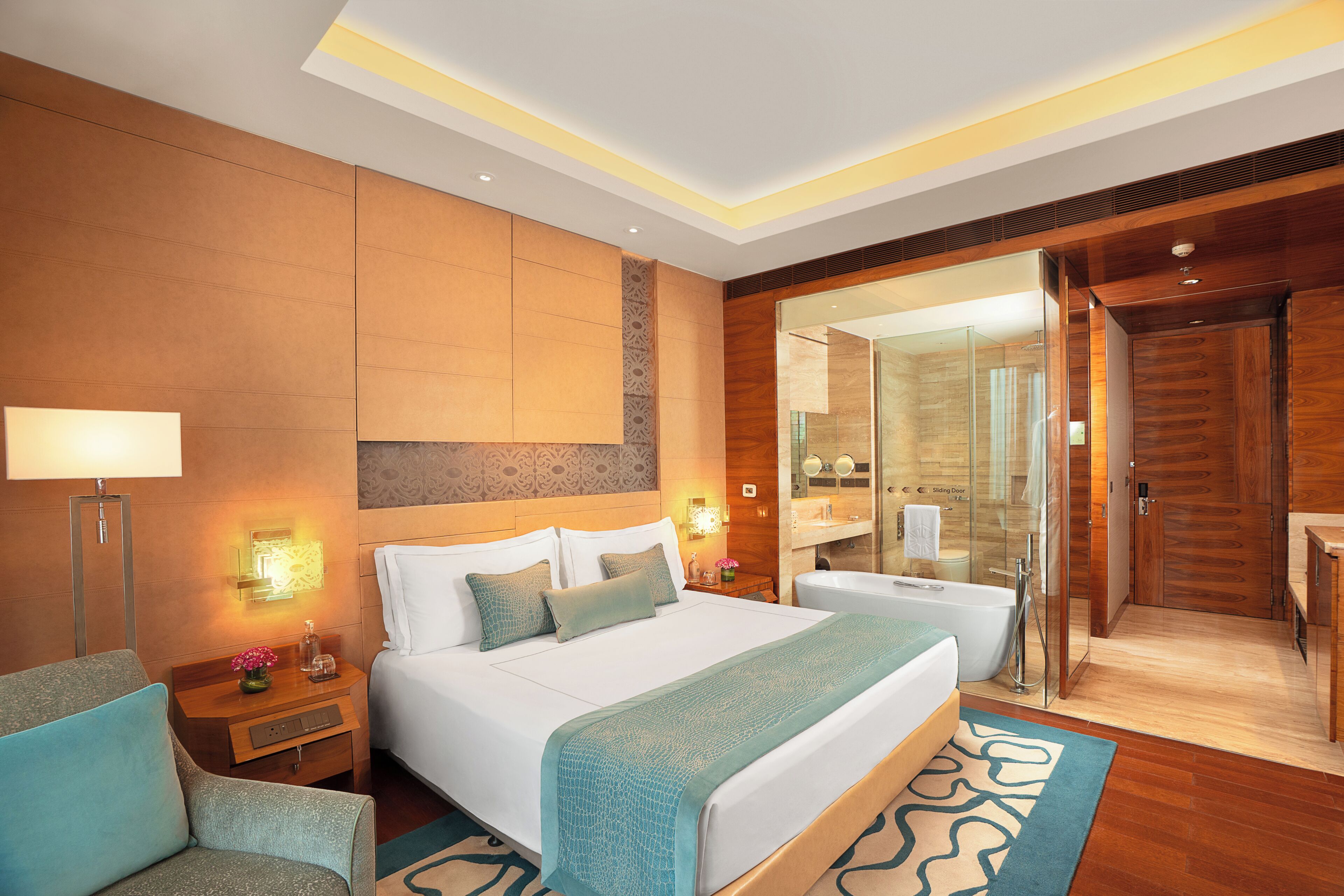 A modern hotel room with a large bed, bedside tables, a mirror, a bathroom with a shower, and a sliding door.