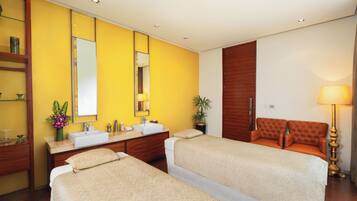 A hotel room with two beds, a large mirror, a wooden wardrobe, a bathroom with a sink, and a bedside table with a lamp.