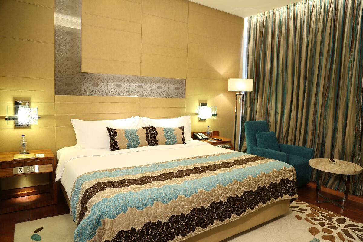 A hotel room with a large bed, a nightstand, a lamp, a chair, and a small table.