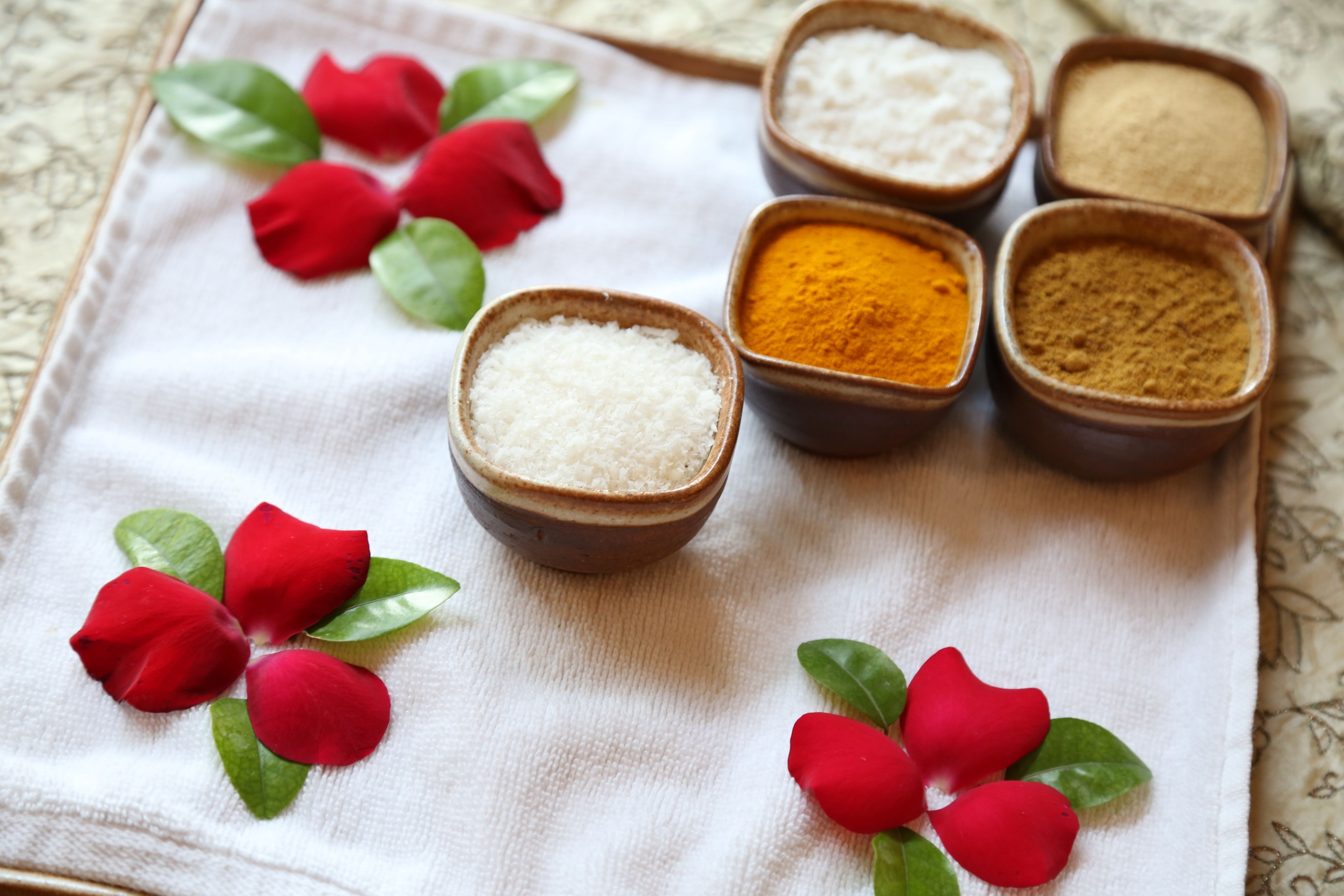 A table with bowls of spices and red flower petals.