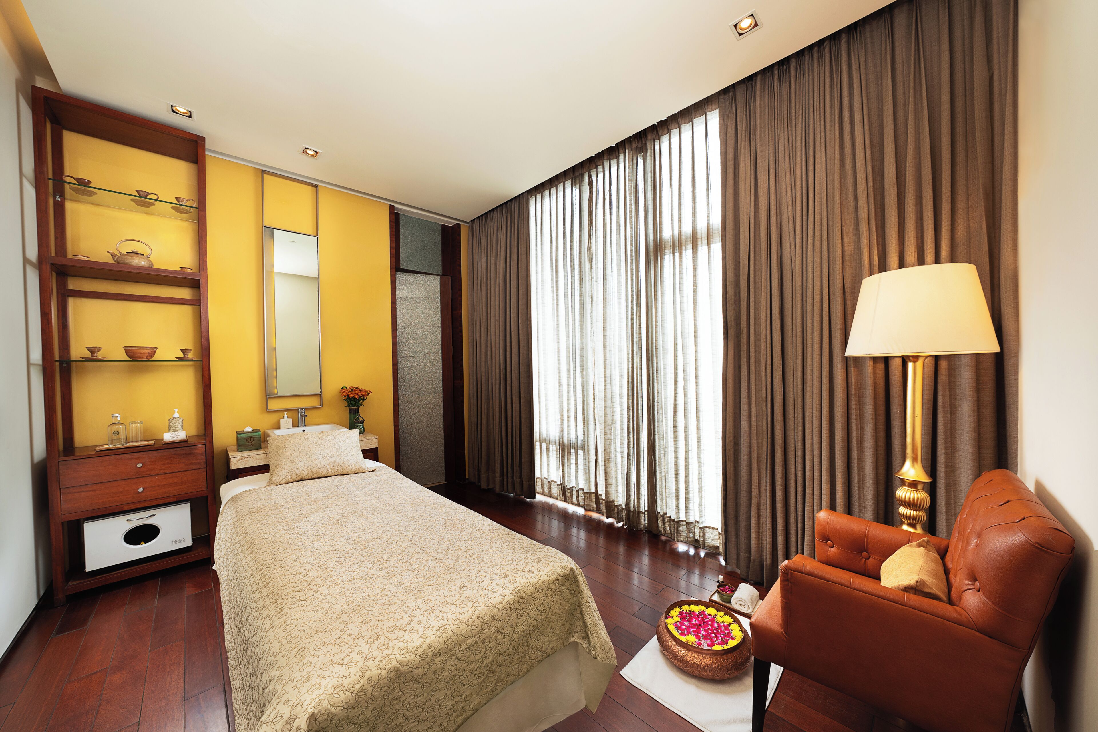 Quarto de hotel com cama, uma cadeira, mesa de cabeceira, espelho e janela com cortinas.