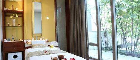 A hotel room with a large bed, a vanity with a mirror, a shelf with toiletries, and a view of greenery outside.