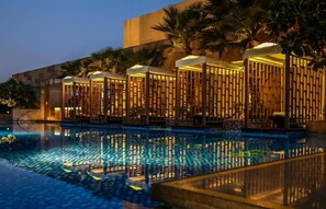 A poolside area with a reflection of a building and palm trees. - Taj City Centre Gurugram (Gurugram)