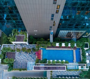 Vista aérea de un edificio moderno con piscina en la azotea, rodeado de vegetación y zonas de estar al aire libre.