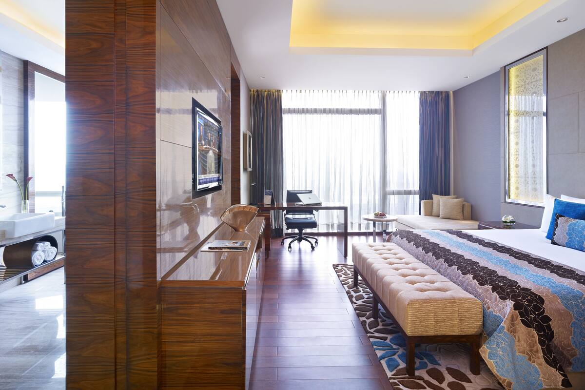 A modern hotel room with a large bed, a sofa, a desk, and a TV mounted on the wall.