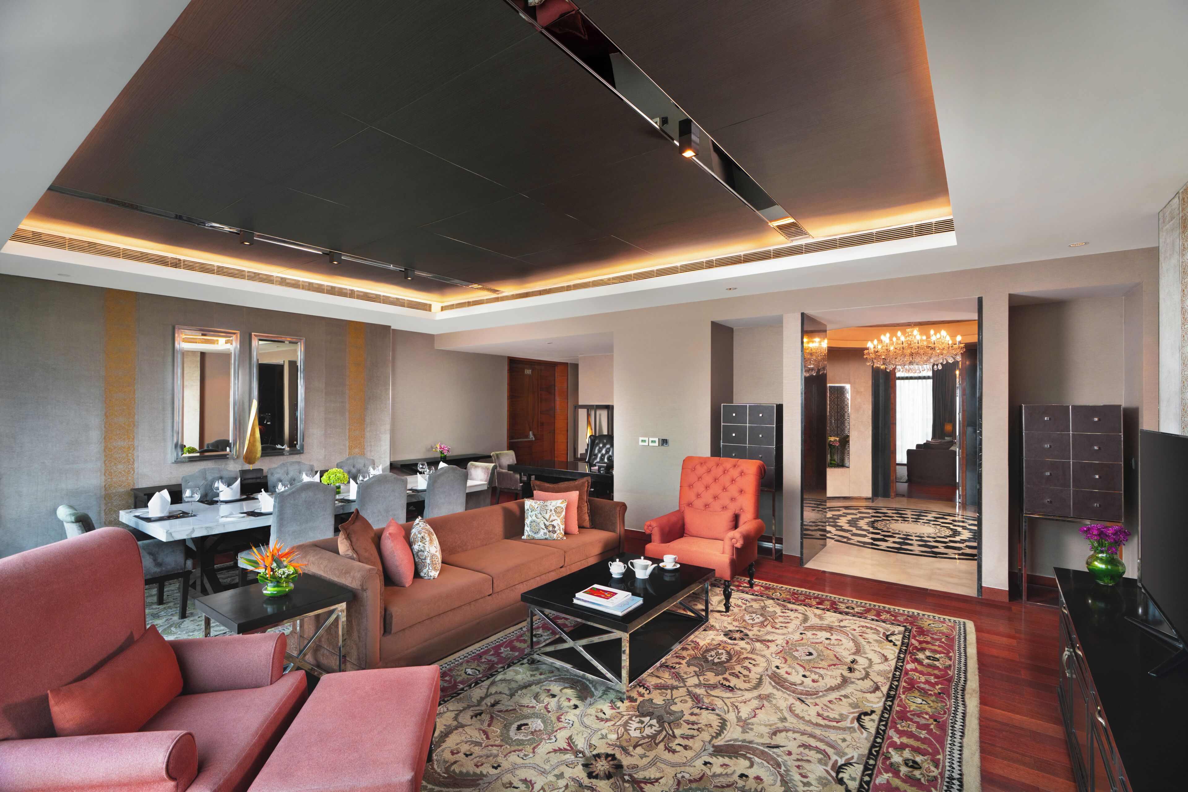 A hotel lobby with a seating area, a dining table, a chandelier, and a patterned carpet.